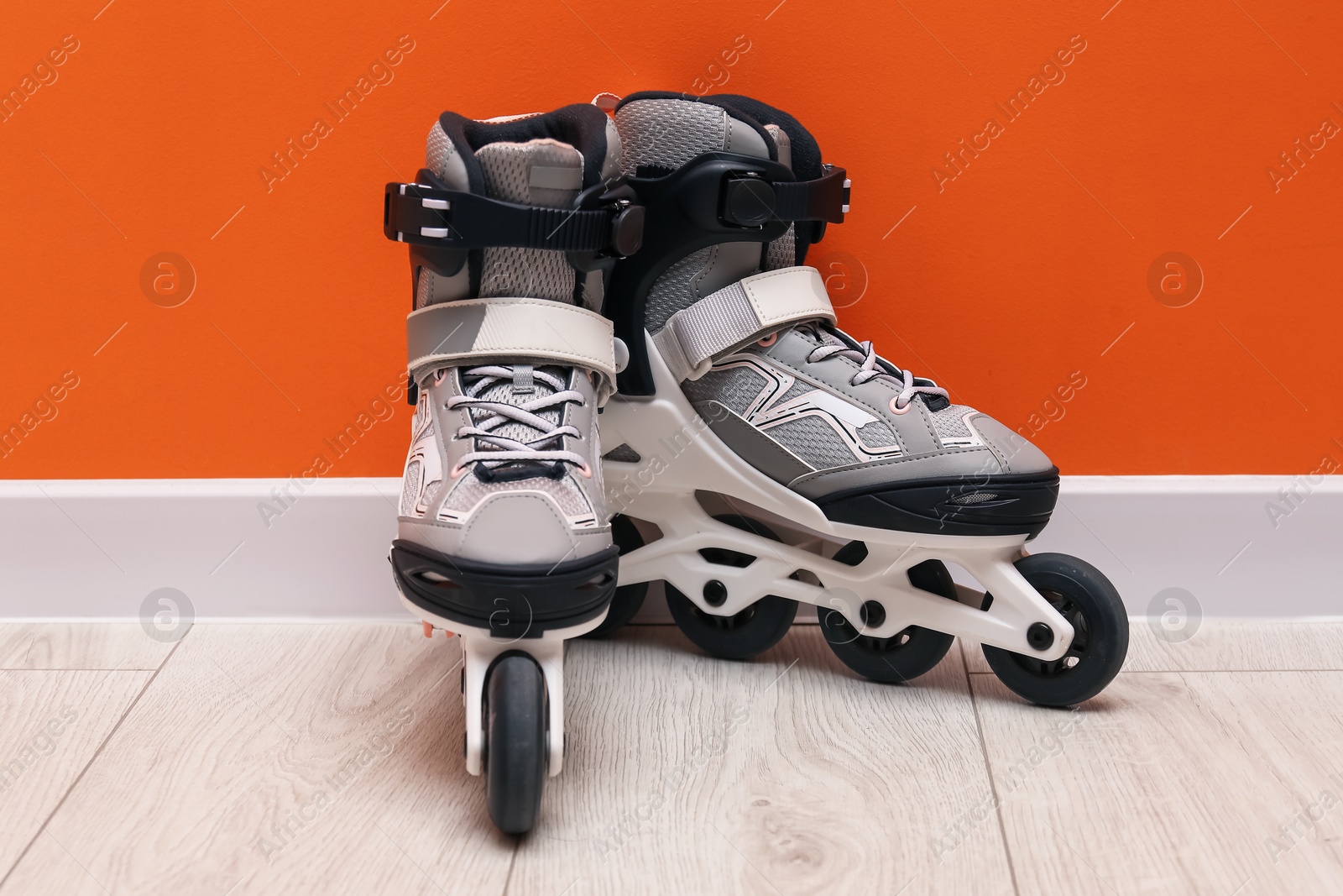 Pair of roller skates on floor near orange wall Photo of Pair of roller skates on floor near orange wall