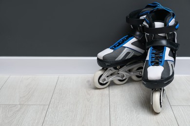 Photo of Pair of roller skates on floor near black wall, space for text