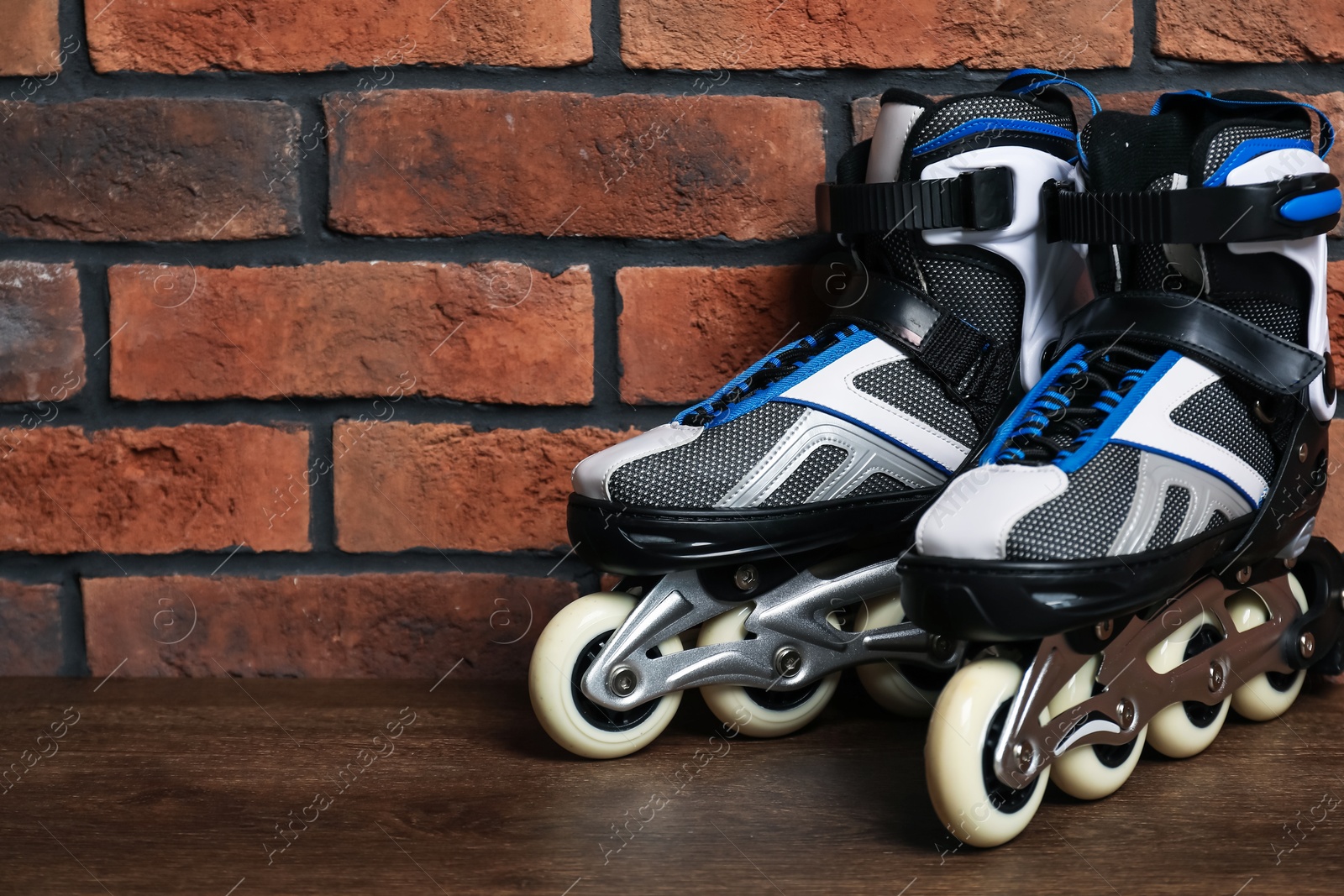 Pair of roller skates on wooden table near brick wall, space for text Photo of Pair of roller skates on wooden table near brick wall, space for text