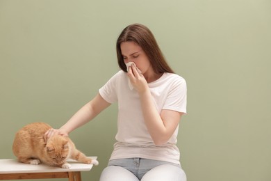Photo of Woman suffering from allergy with her cat near green wall indoors