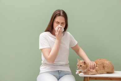Photo of Woman suffering from allergy with her cat near green wall indoors