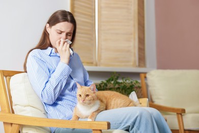Photo of Woman suffering from allergy with her cat in armchair at home