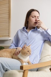 Photo of Woman suffering from allergy with her cat in armchair at home
