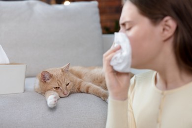Photo of Woman suffering from allergy with her cat at home, selective focus