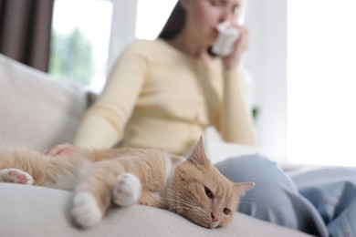 Photo of Woman suffering from allergy with her cat on sofa at home, selective focus