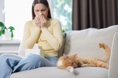 Photo of Woman suffering from allergy with her cat on sofa at home, selective focus