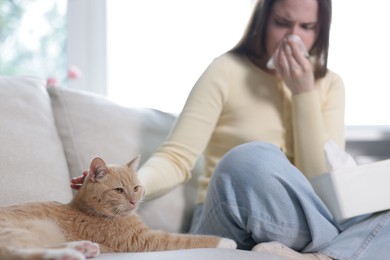 Photo of Woman suffering from allergy with her cat on sofa at home, selective focus
