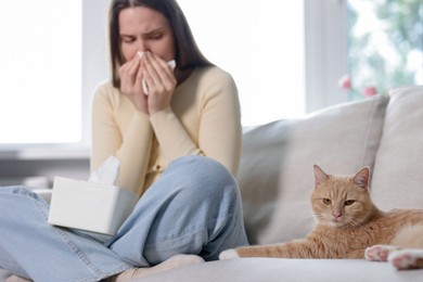 Photo of Woman suffering from allergy with her cat on sofa at home, selective focus
