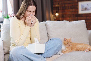 Photo of Woman suffering from allergy with her cat on sofa at home