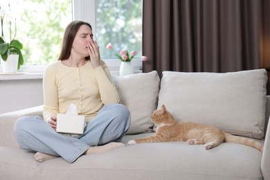 Photo of Woman suffering from allergy with her cat on sofa at home
