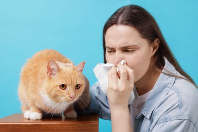 Photo of Woman suffering from allergy with her cat on light blue background