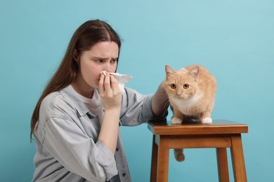 Photo of Woman suffering from allergy with her cat on light blue background