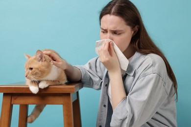 Photo of Woman suffering from allergy with her cat on light blue background