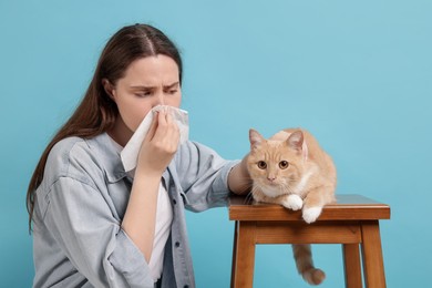 Photo of Woman suffering from allergy with her cat on light blue background
