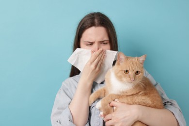 Photo of Woman suffering from allergy with her cat on light blue background