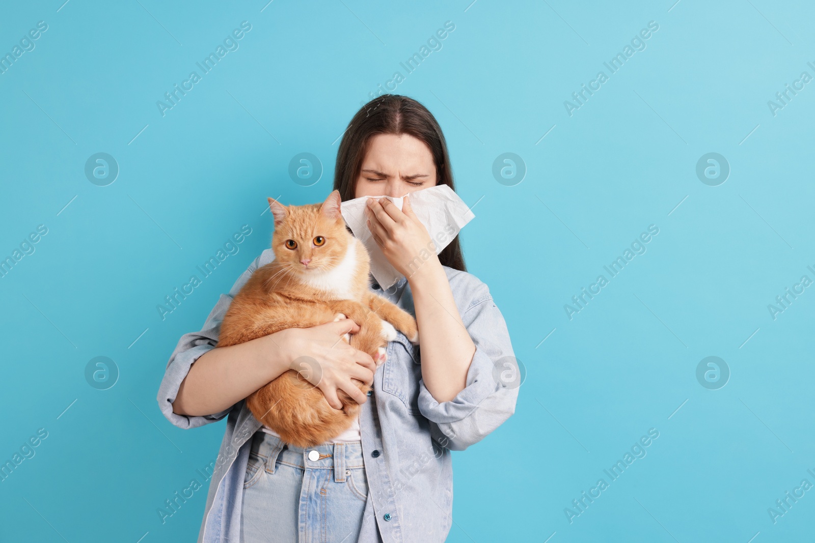 Woman suffering from allergy with her cat on light blue background Photo of Woman suffering from allergy with her cat on light blue background