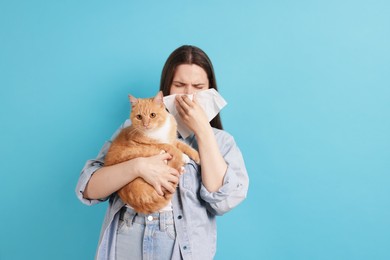 Photo of Woman suffering from allergy with her cat on light blue background