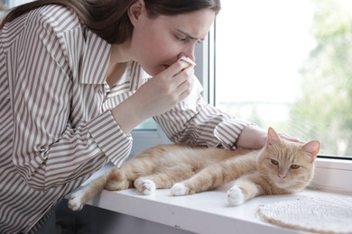 Photo of Woman suffering from allergy with her cat near window at home