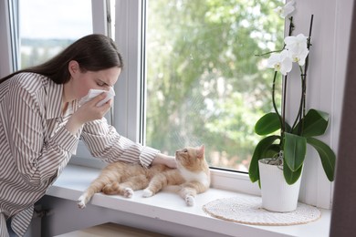 Photo of Woman suffering from allergy with her cat near window at home