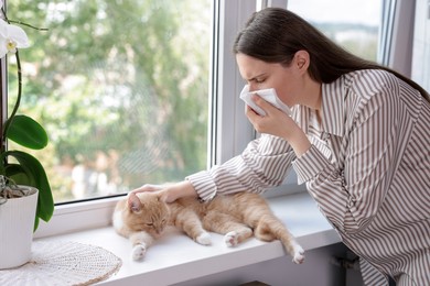 Photo of Woman suffering from allergy with her cat near window at home
