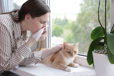 Photo of Woman suffering from allergy with her cat near window at home