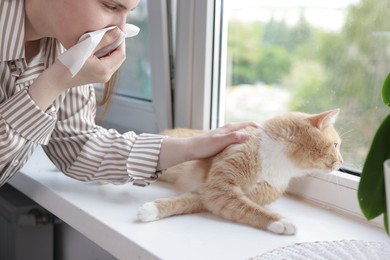 Photo of Woman suffering from allergy with her cat near window at home, closeup