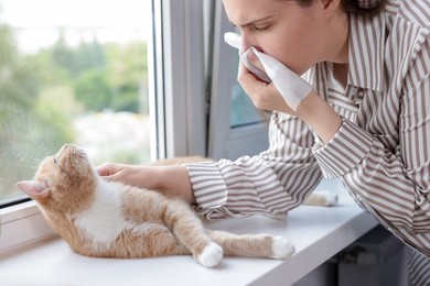 Photo of Woman suffering from allergy with her cat near window at home, closeup