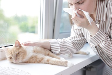 Photo of Woman suffering from allergy with her cat near window at home, closeup