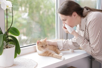 Photo of Woman suffering from allergy with her cat near window at home