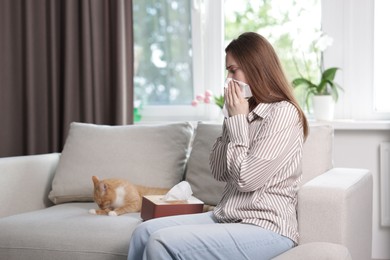 Photo of Woman suffering from allergy with her cat on sofa at home