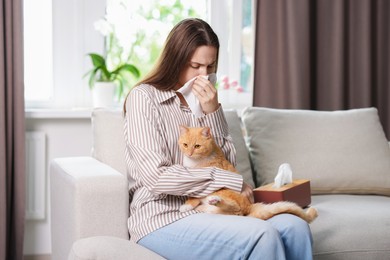 Photo of Woman suffering from allergy with her cat on sofa at home
