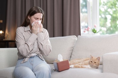 Photo of Woman suffering from allergy with her cat on sofa at home