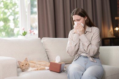 Photo of Woman suffering from allergy with her cat on sofa at home