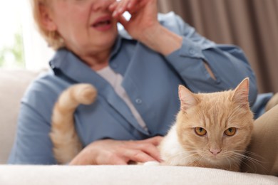 Photo of Senior woman suffering from allergy with her cat on sofa at home, closeup