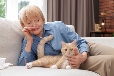 Photo of Senior woman suffering from allergy with her cat on sofa at home