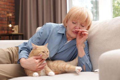 Photo of Senior woman suffering from allergy with her cat on sofa at home