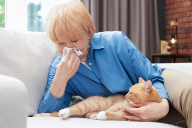 Photo of Senior woman suffering from allergy with her cat on sofa at home