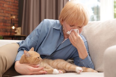 Photo of Senior woman suffering from allergy with her cat on sofa at home