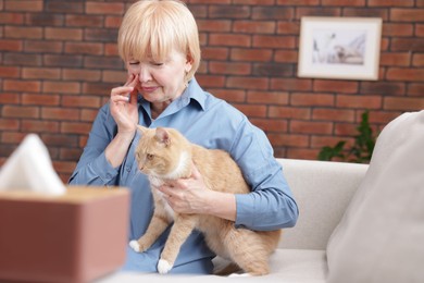 Photo of Senior woman suffering from allergy with her cat on sofa at home
