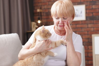 Photo of Senior woman suffering from allergy with her cat on sofa at home