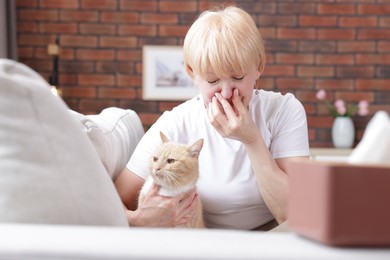 Photo of Senior woman suffering from allergy with her cat on sofa at home