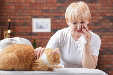 Photo of Senior woman suffering from allergy with her cat on sofa at home