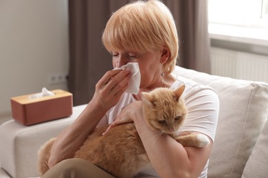 Photo of Senior woman suffering from allergy with her cat on sofa at home