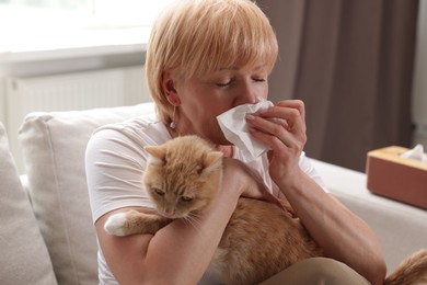 Photo of Senior woman suffering from allergy with her cat on sofa at home
