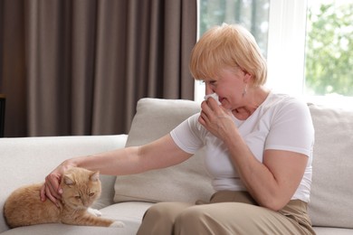 Photo of Senior woman suffering from allergy with her cat on sofa at home