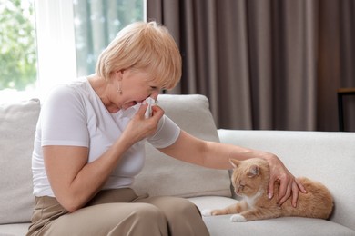Photo of Senior woman suffering from allergy with her cat on sofa at home