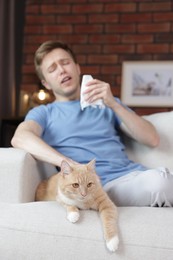 Photo of Man suffering from allergy with his cat on sofa at home, selective focus