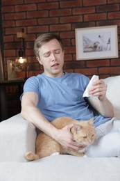 Photo of Man suffering from allergy with his cat on sofa at home