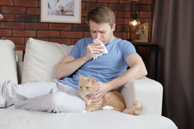 Photo of Man suffering from allergy with his cat on sofa at home
