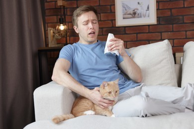 Photo of Man suffering from allergy with his cat on sofa at home